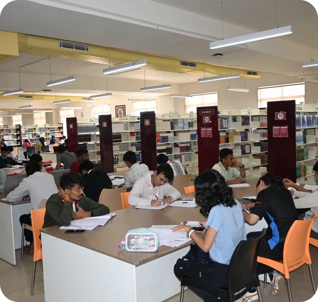 Students studying at library tables with bookshelves